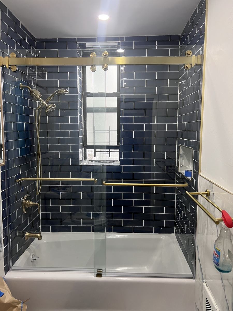 Frameless sliding tub enclosure with brushed gold hardware
