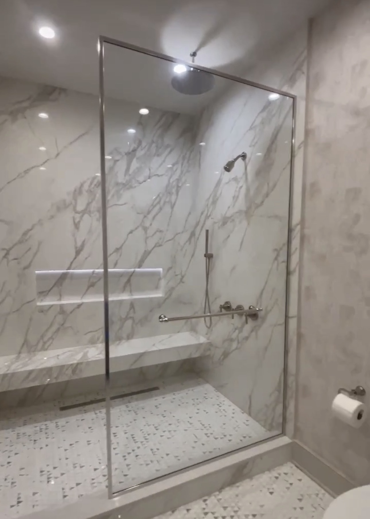 Frameless fixed glass splashguard panel in a marble-tile walk-in shower