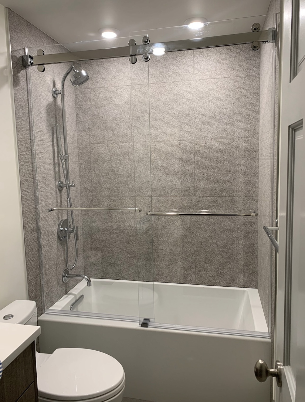 Frameless sliding glass tub and shower enclosure with chrome hardware and gray tile walls