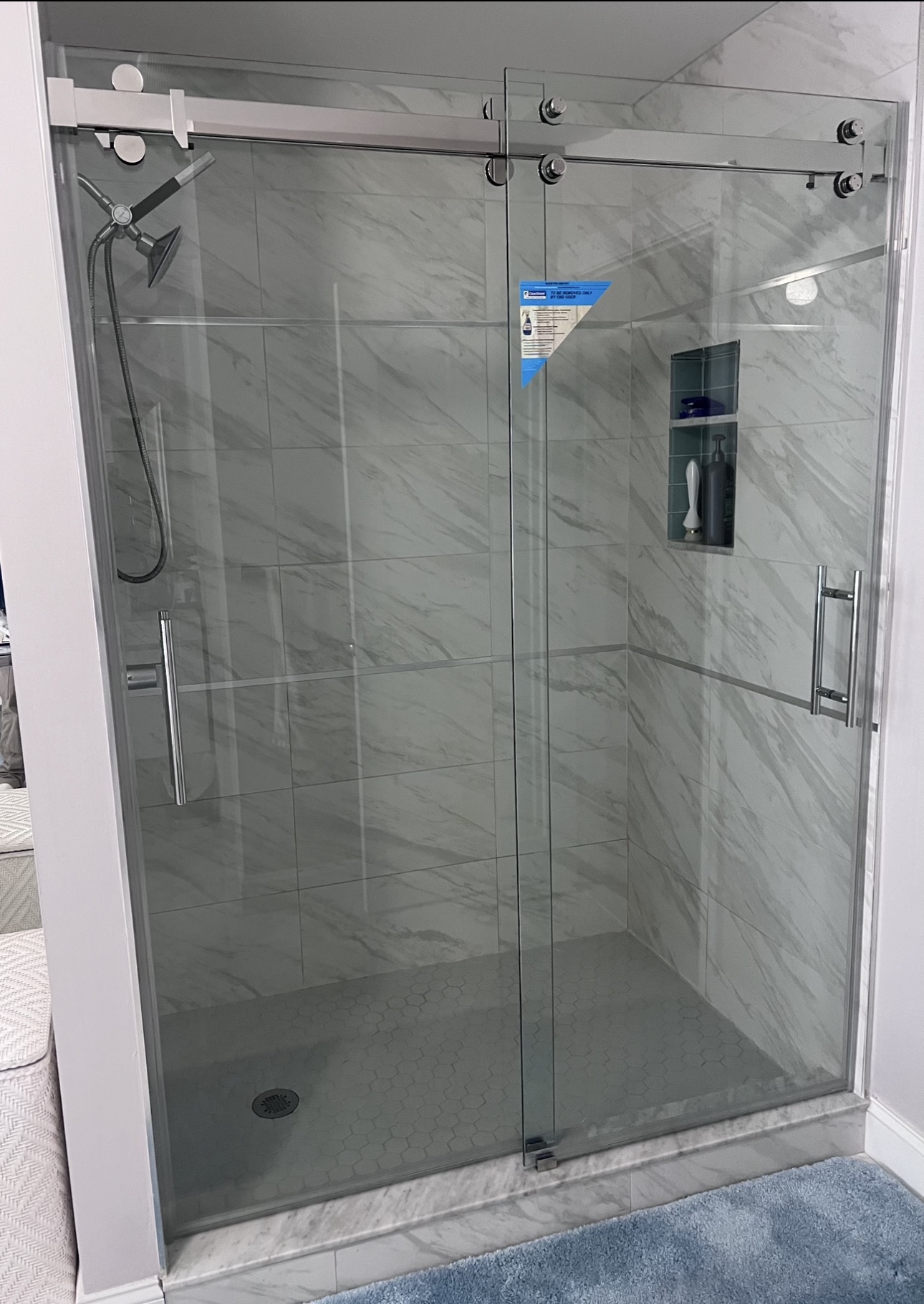 Frameless two-door sliding shower enclosure with a top rail and marble-look tile